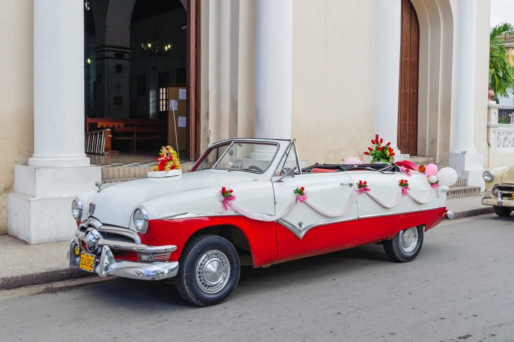 Old-fashioned car decorated with flowers and ribbon parked in front of a building.