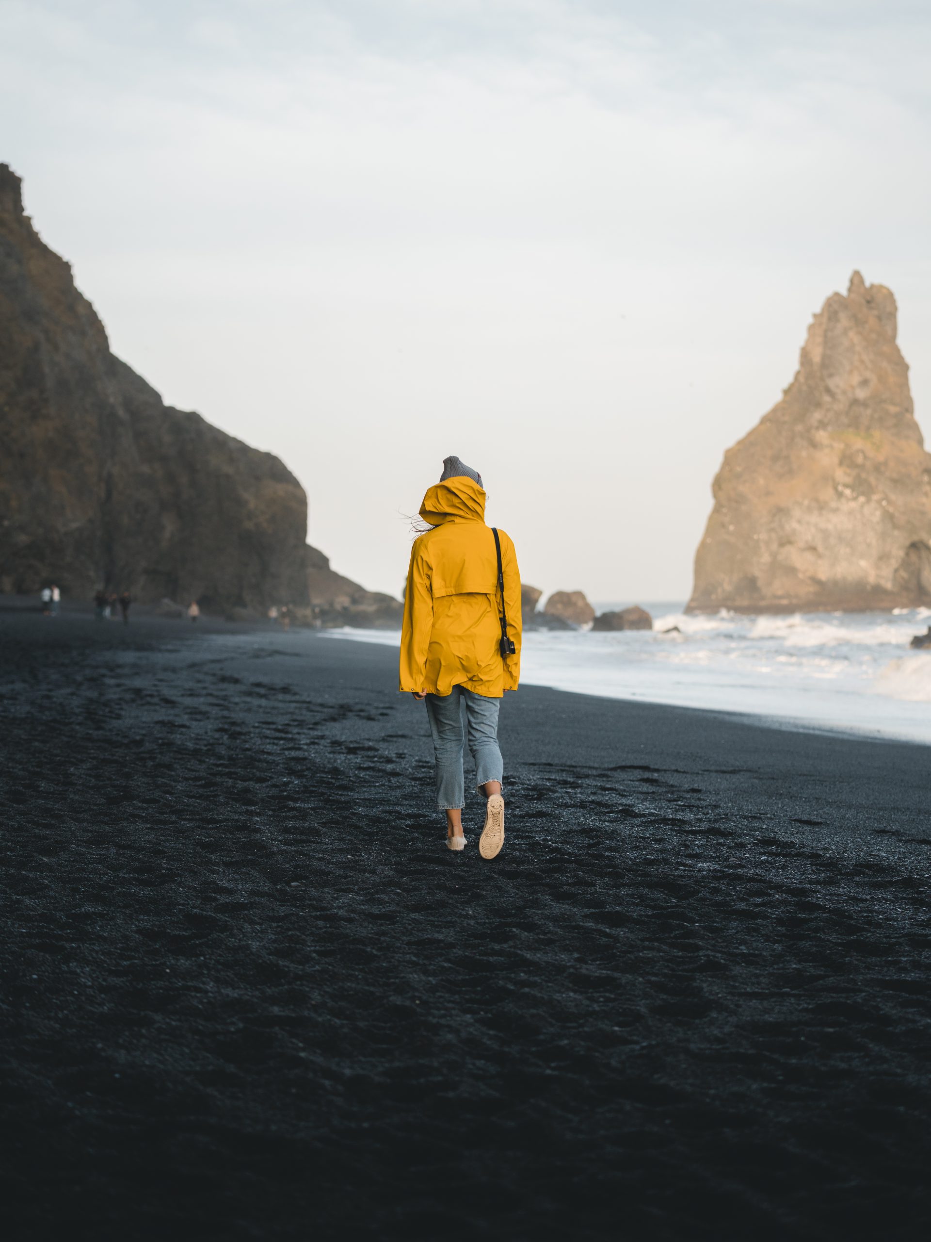 A woman in a yellow raincoat walking on a black sand beach