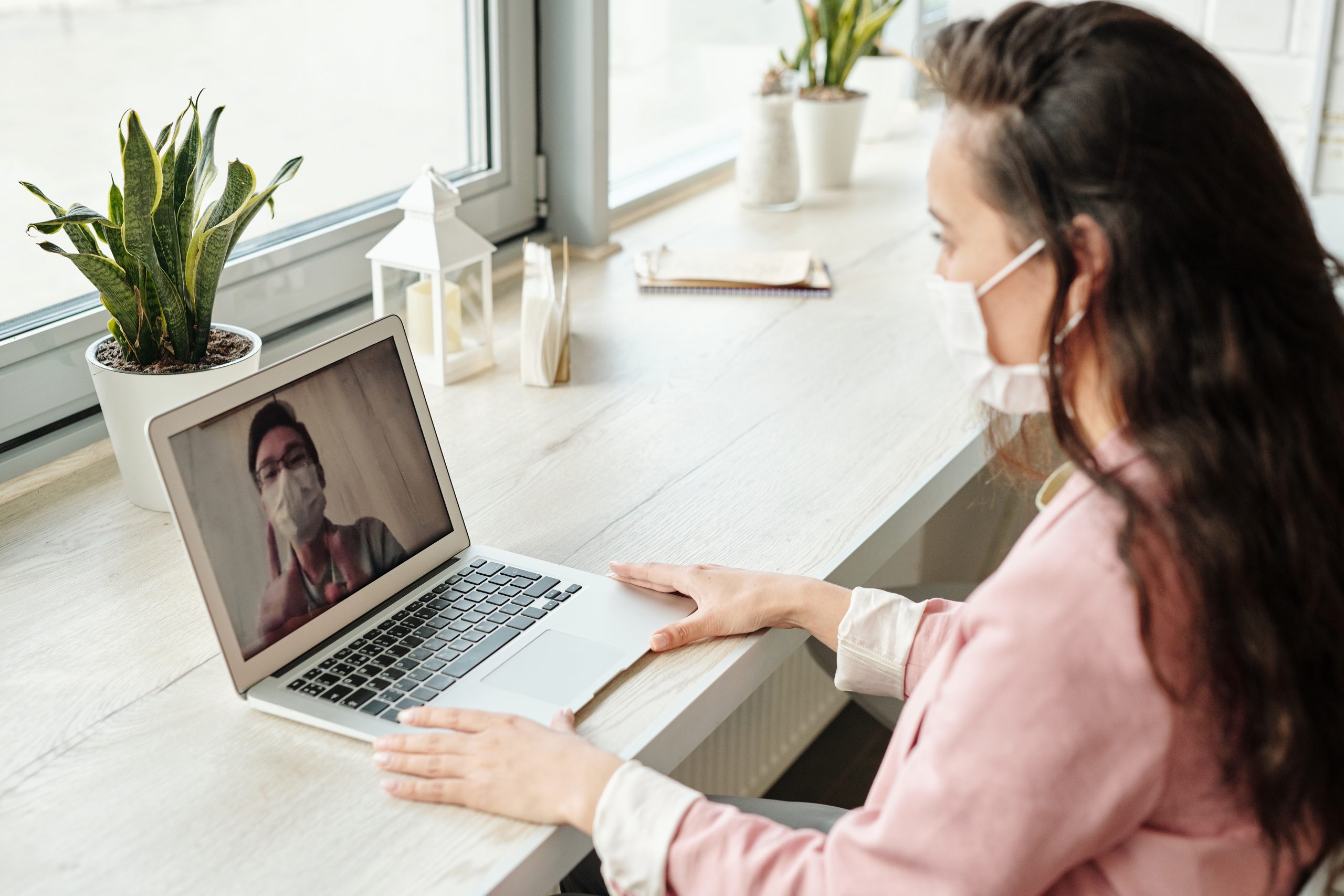 Person wearing a mask and talking to another person on their laptop.