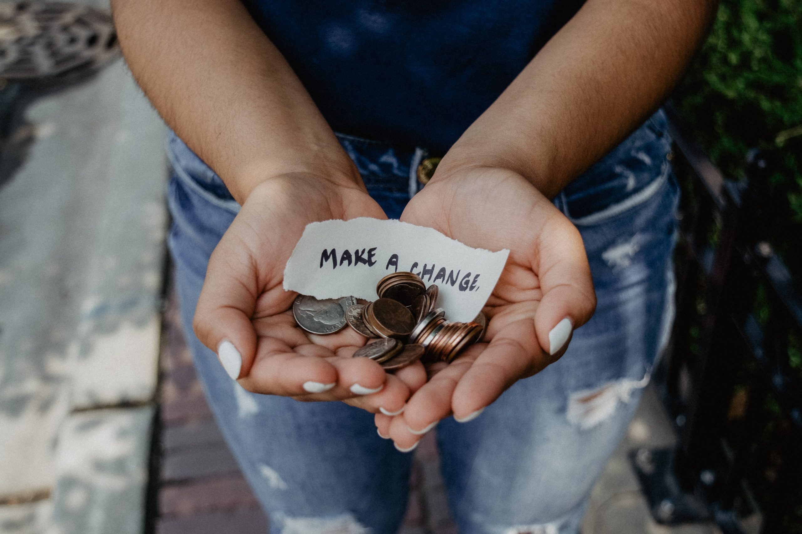 person holding coins in their hands with note that reads "make a change"