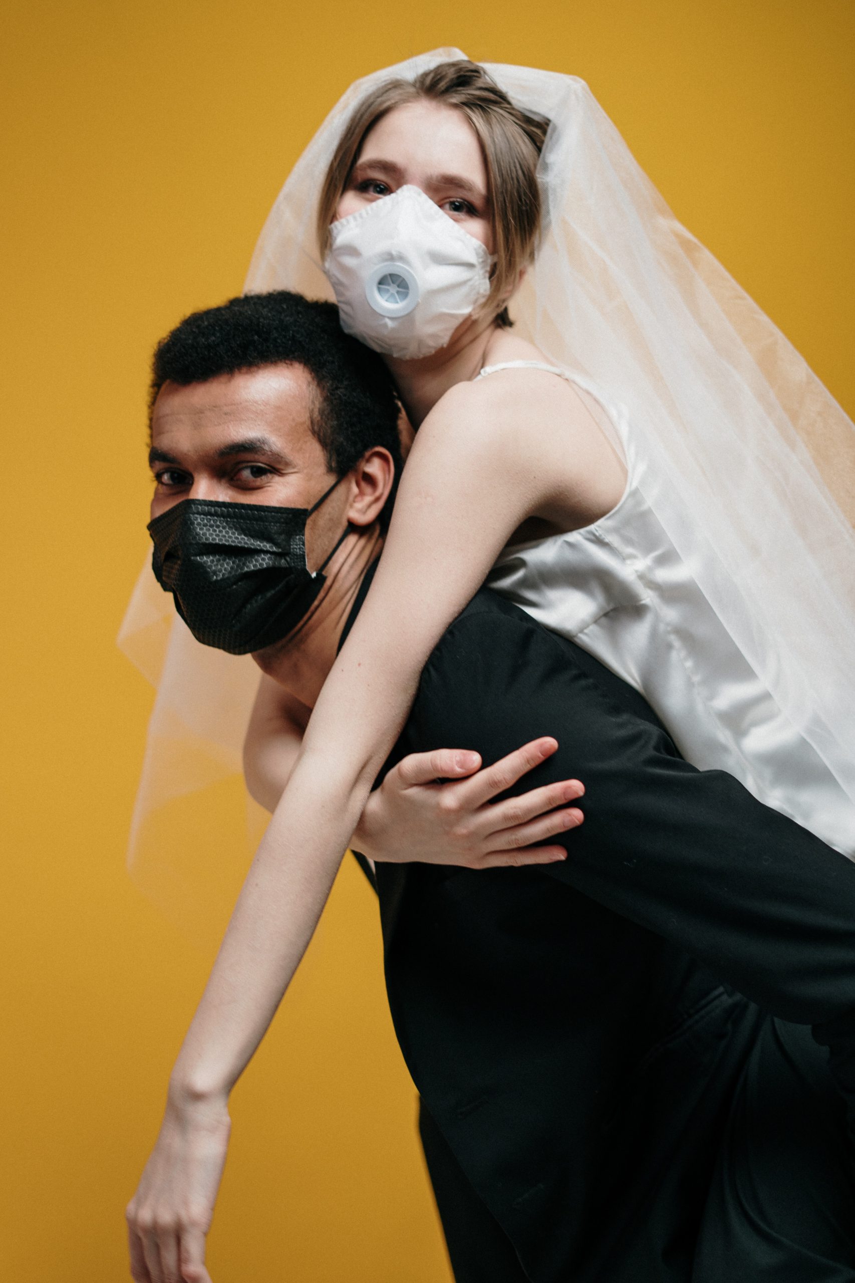 Groom and bride wearing masks and giving a piggy back ride.