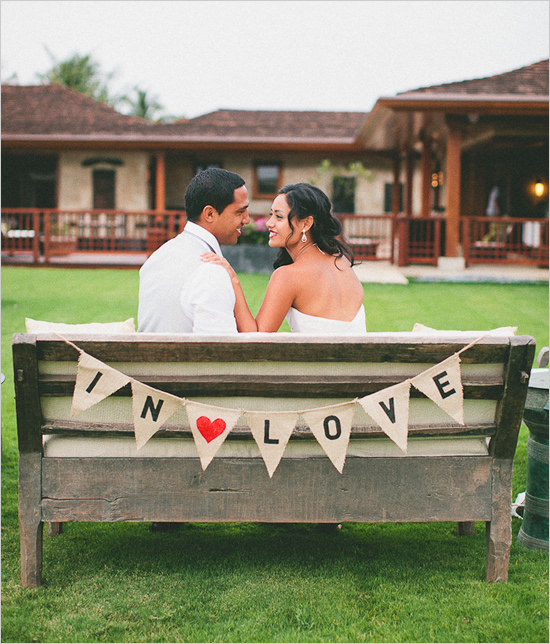 Couple sitting next to each other on a bench with a banner that says "In *heart* love."