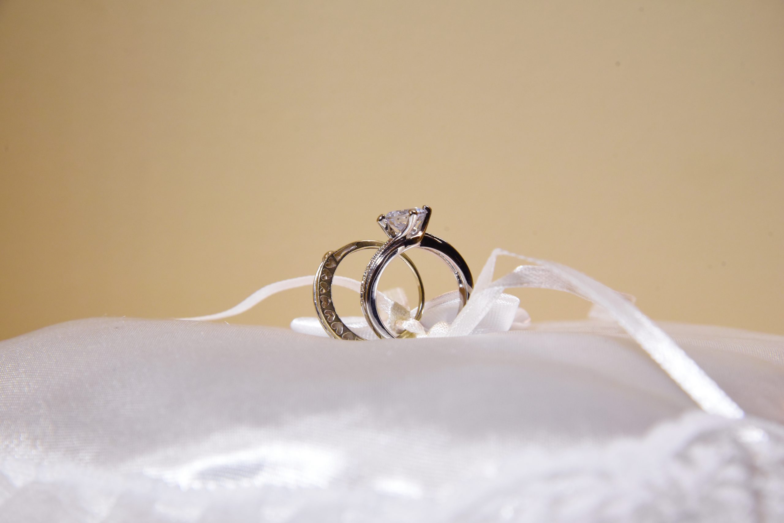 Two diamond wedding rings sitting in the center of a white satin cushion.