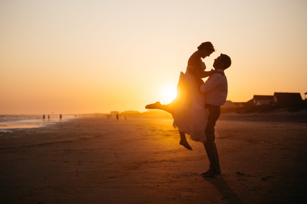 a couple on a beach with man lifting up woman