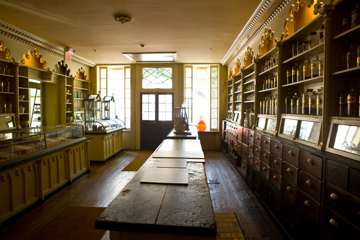 dimly lit apothecary room with lots of shelving and glass display cases of bottles